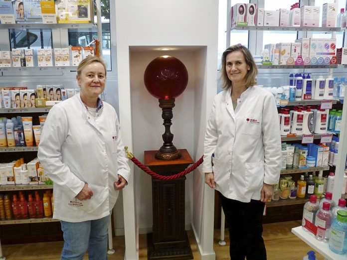 Silvia (izda.) y Nuria Campoamor (dcha.) junto a la bola de cristal que en el siglo XIX se ponía en el escaparate para indicar que el local era una farmacia