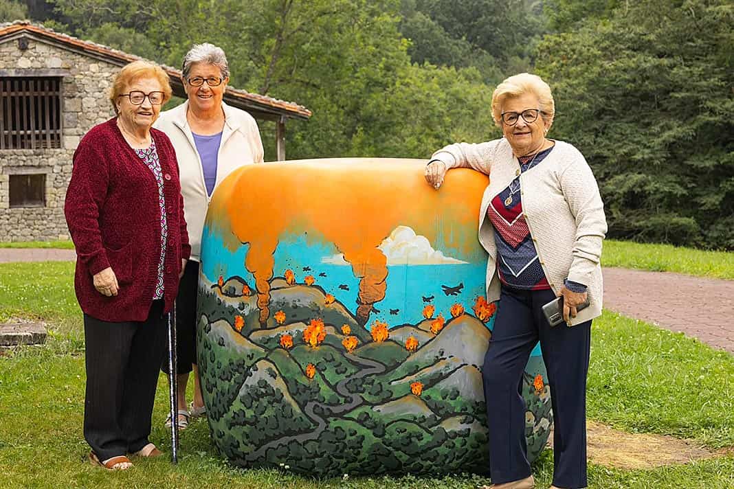 Tres vecinas, Saramari, Tini y Josefina posan junto a la pintura que rememora un episodio histórico que formó parte de sus vidas: la batalla del Mazucu. Artista: Guillermo Menéndez Quirós @punkillismo