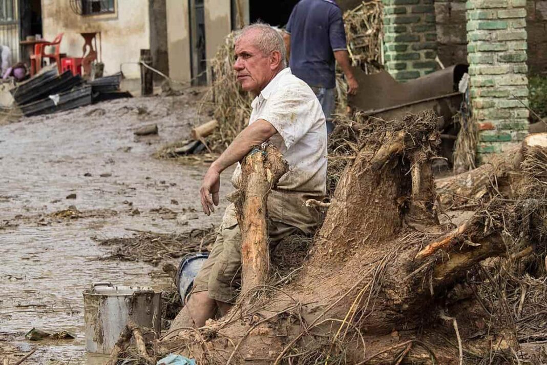 Hombre sentado a la entrada de su casa tras una inundación causada por un desastre natural