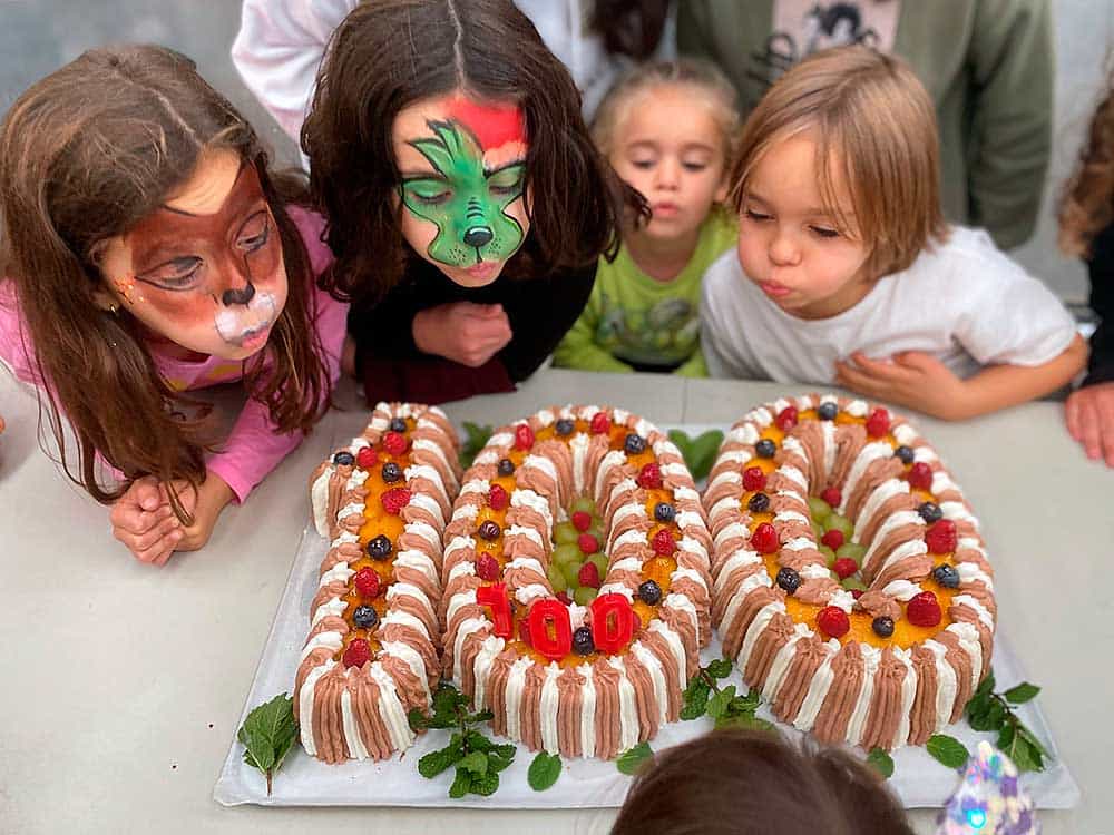 Carmen, Triana, Olaya y Roberto soplando las velas de la tarta conmemorativa del Centenario de la escuela rural de Valdepares.