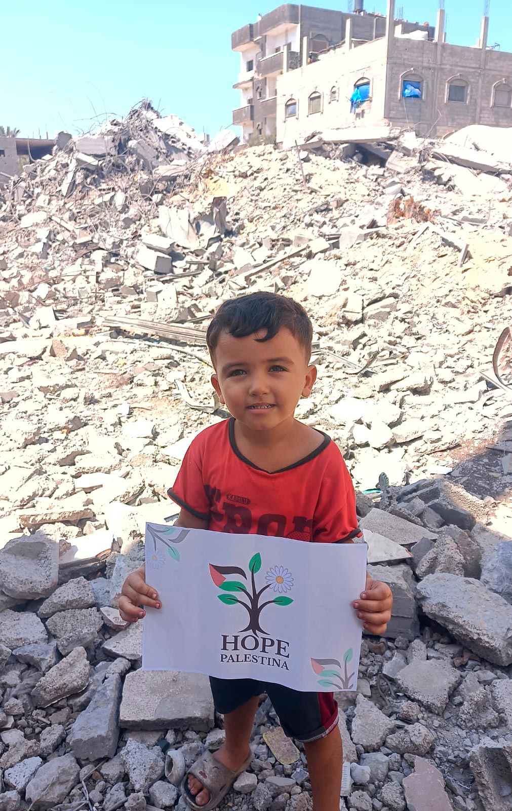 Niño palestino entre los escombros de Gaza con un cartel de Hope Palestina.