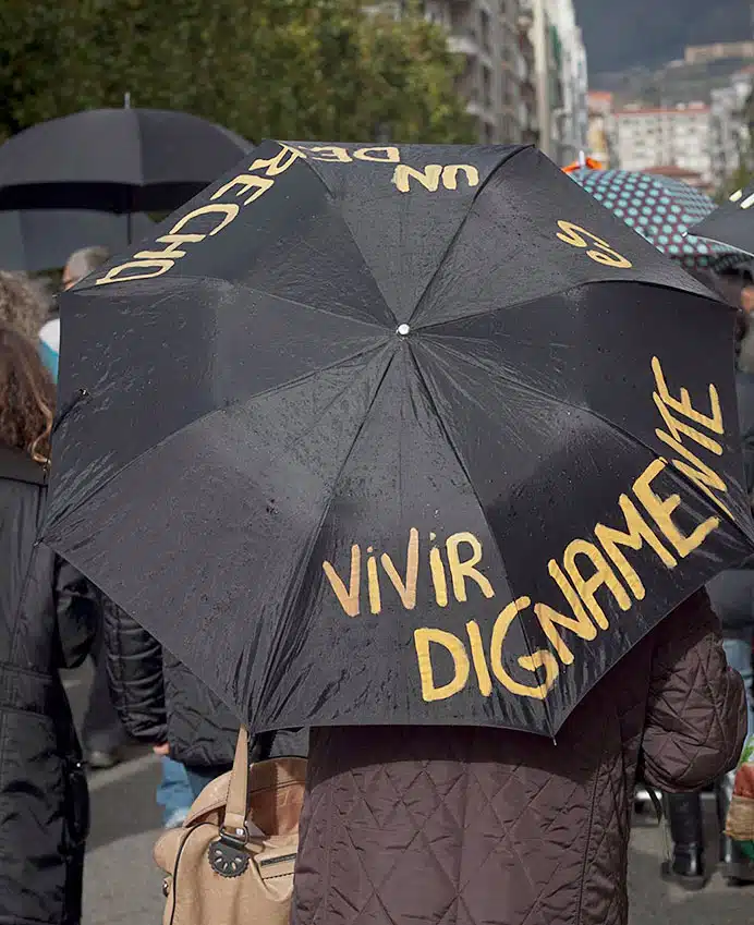 Persona con un paragua donde se puede leer 'Vivir dignamente es un derecho'